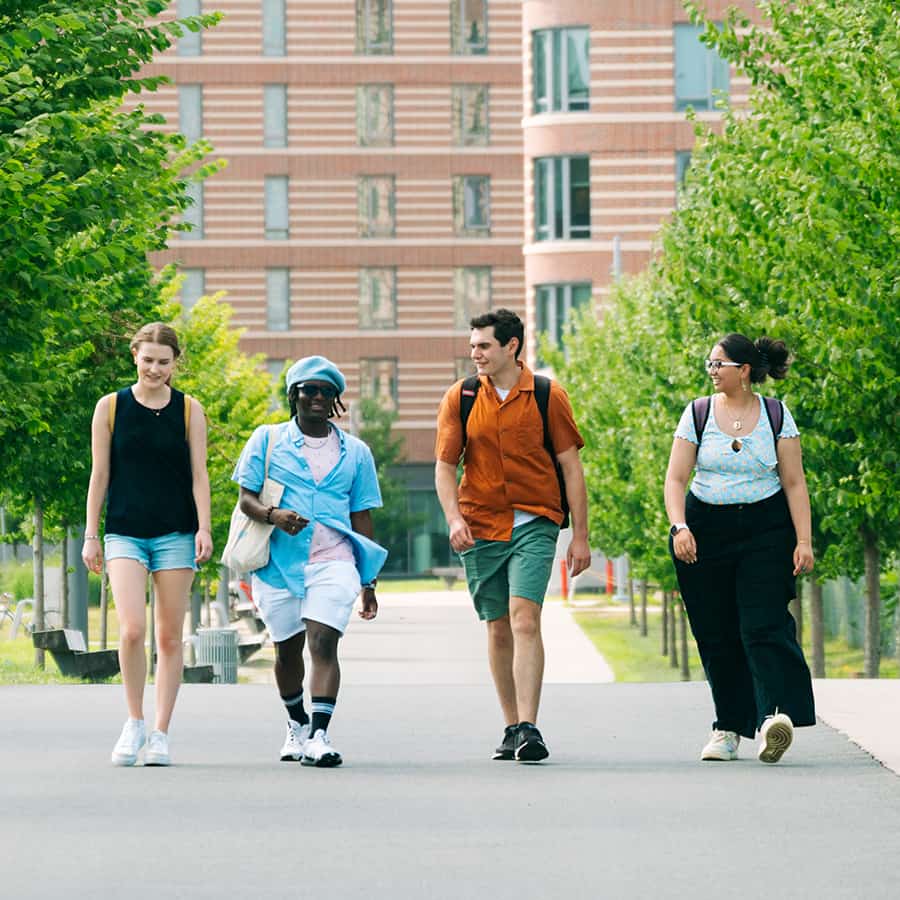 Four students walking on paved path in front of trees and building.