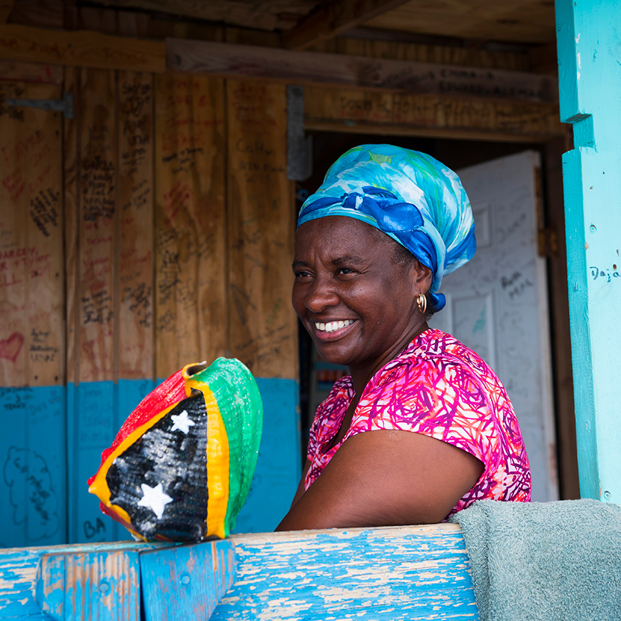 Cockleshell Beach, Saint Kitts and Nevis - November 16, 2015: A woman sits outside a rustic building at Cockleshell Beach on the Caribbean island of St. Kitts. The shell is painted with the flag of St. Kitts and Nevis.